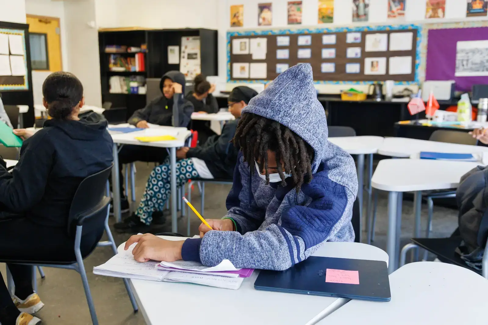 Student writing with pencil in notebook at classroom desk