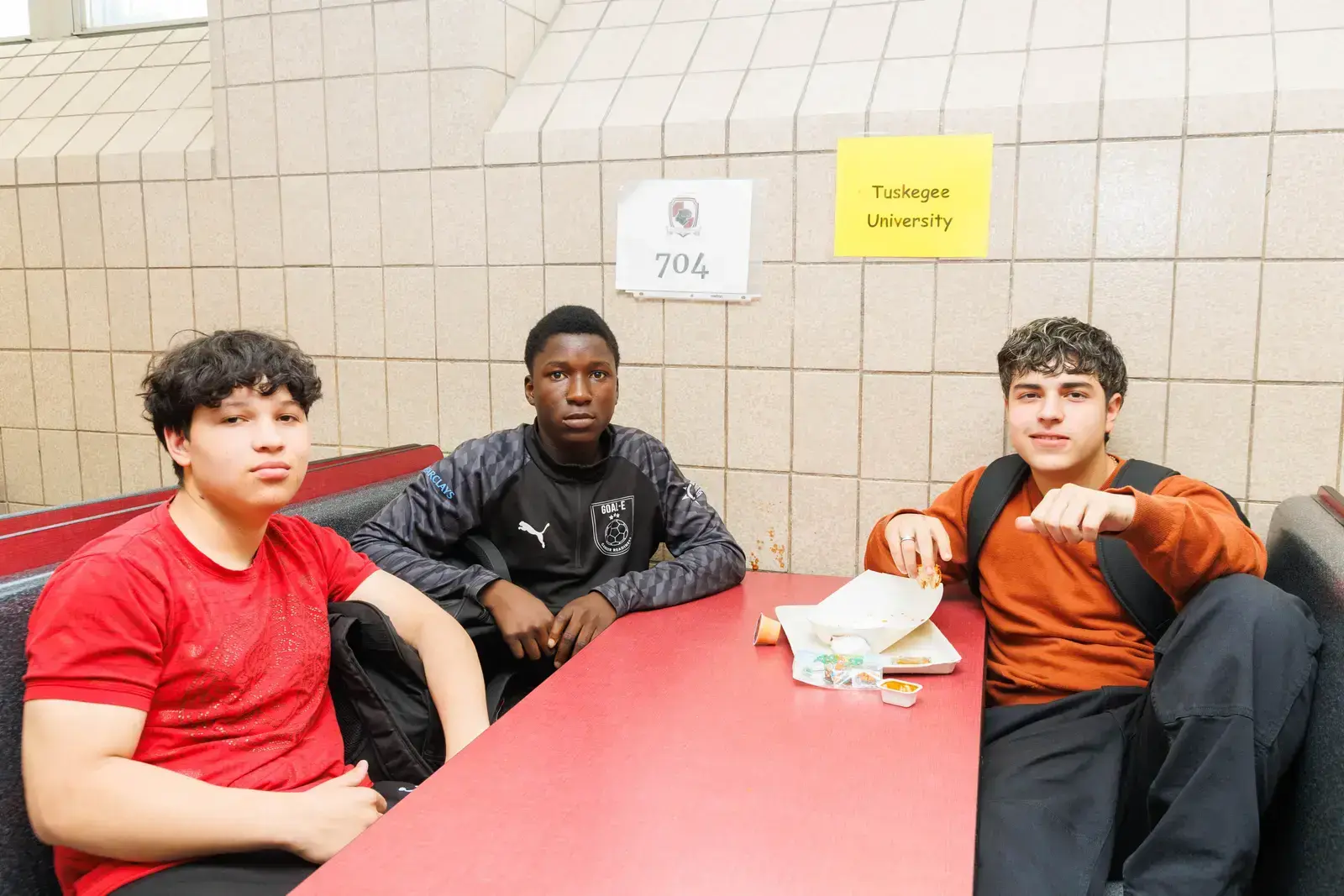 Three male students eating lunch together at school cafeteria table