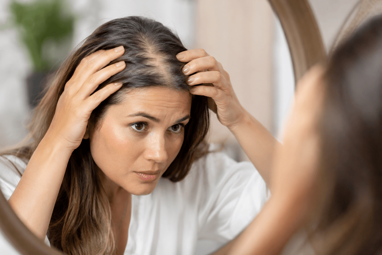 Woman examining thinning hair in mirror in San Diego California before hair restoration treatment