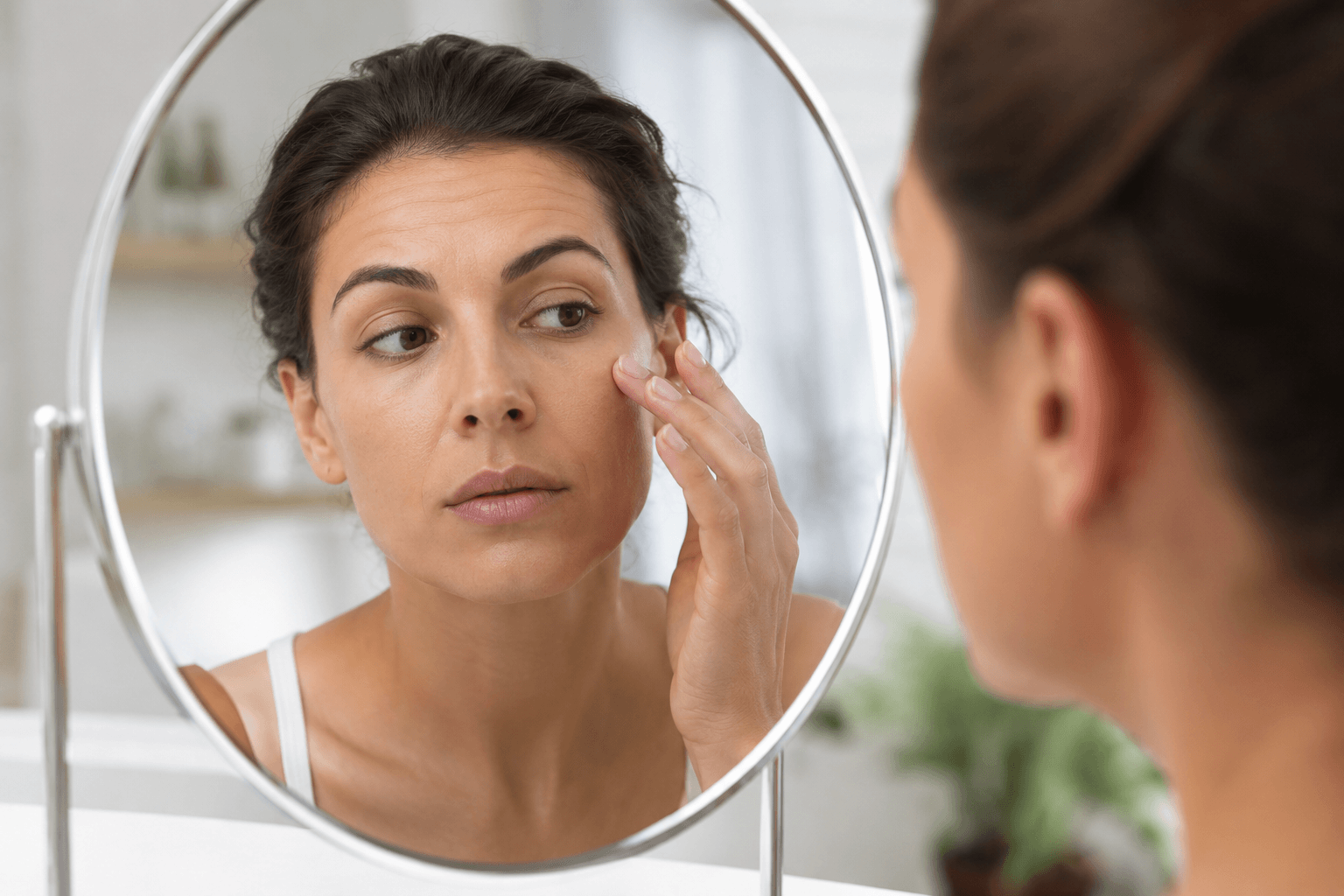 Woman examining subtle facial volume loss and early signs of aging before considering facial fillers in La Mesa California
