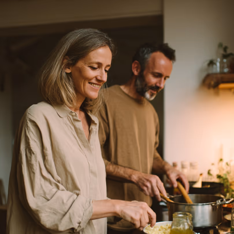 Smiling couple cooking together in a warm, cozy kitchen.