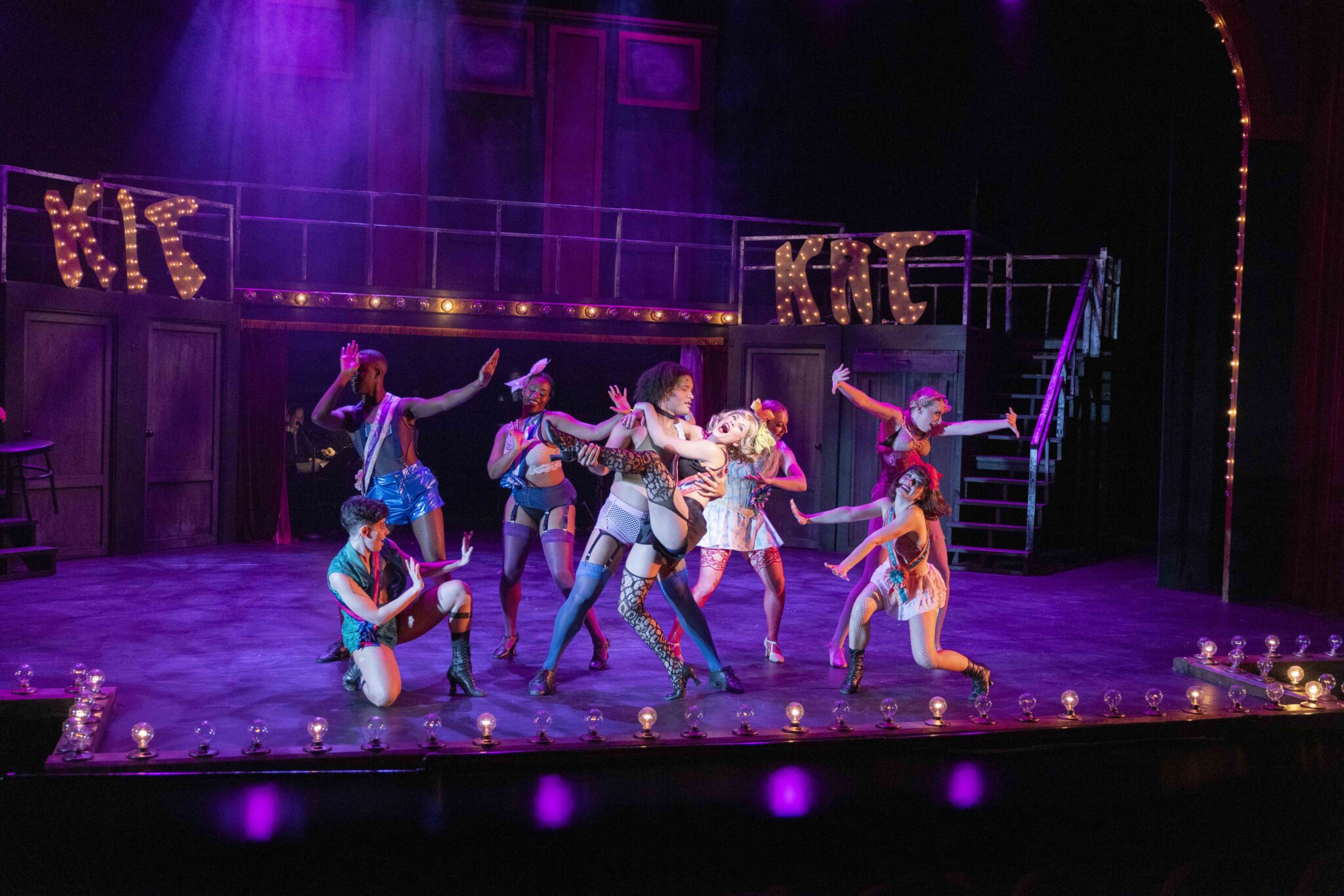 Performers in colorful costumes dance on a lit stage with 'KTC' lighted signs in the background.