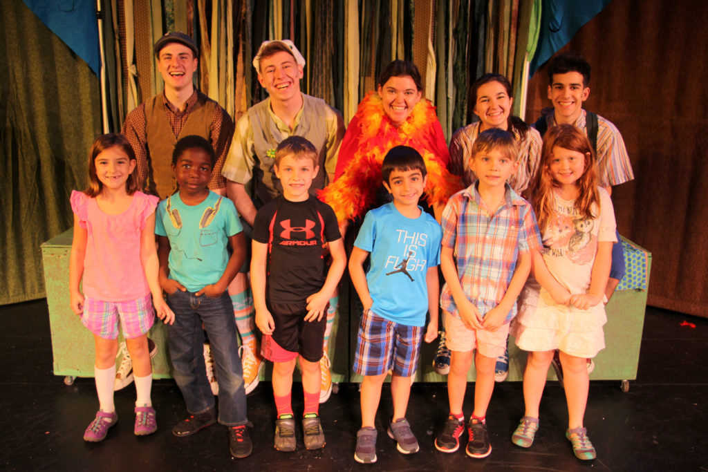 Group of smiling children and young adults posing on stage in colorful clothes and costumes.