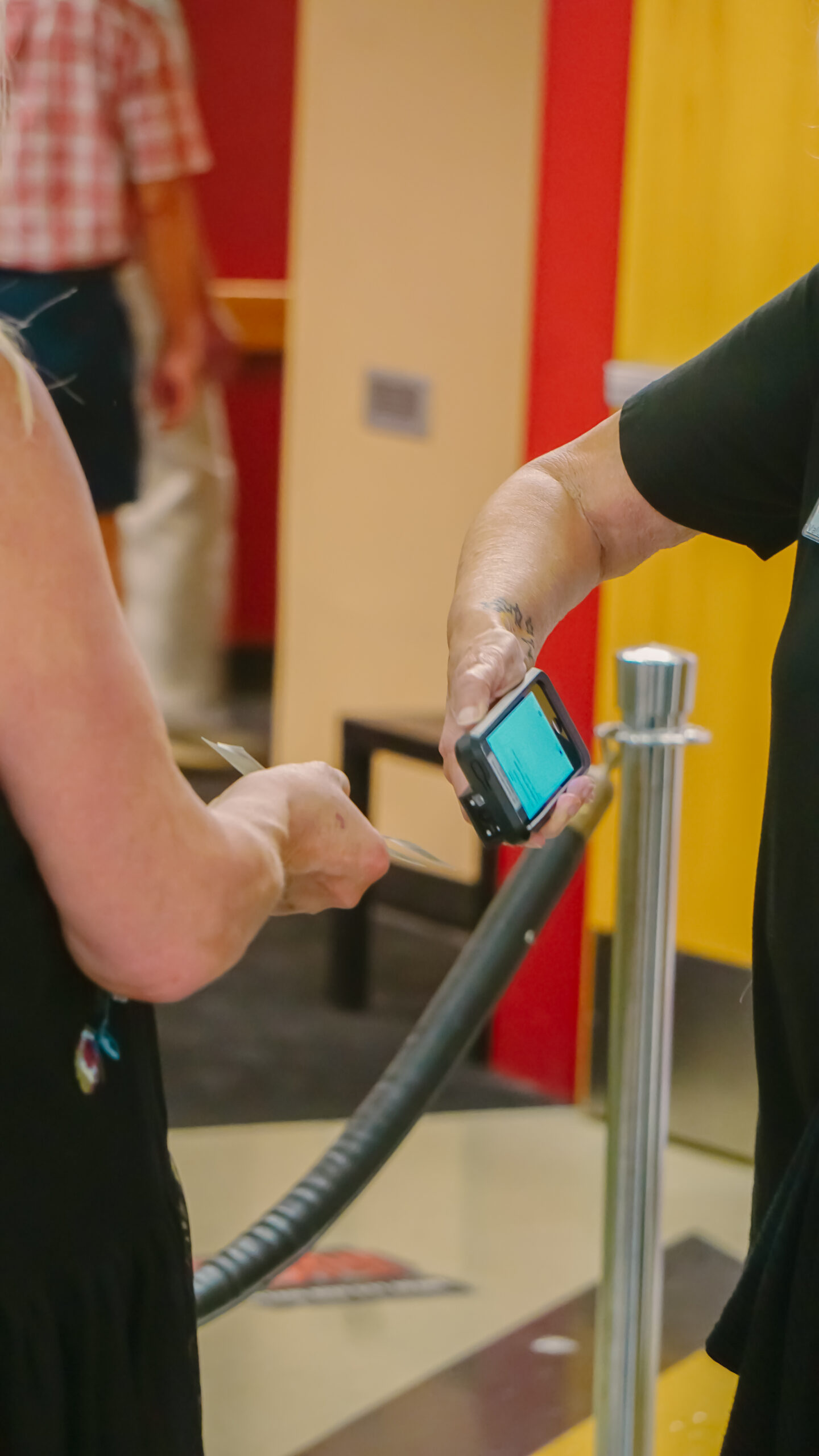 Person scanning ticket or pass on a handheld device at an entry point with a queue rope.