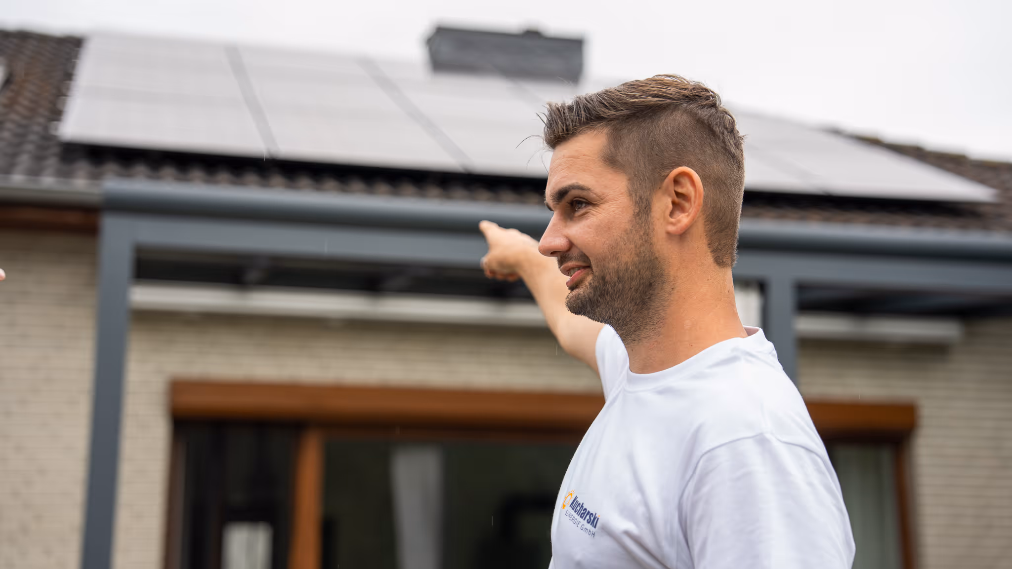 Mann zeigt auf Solarpaneele auf dem Dach eines Hauses an einem bewölkten Tag.