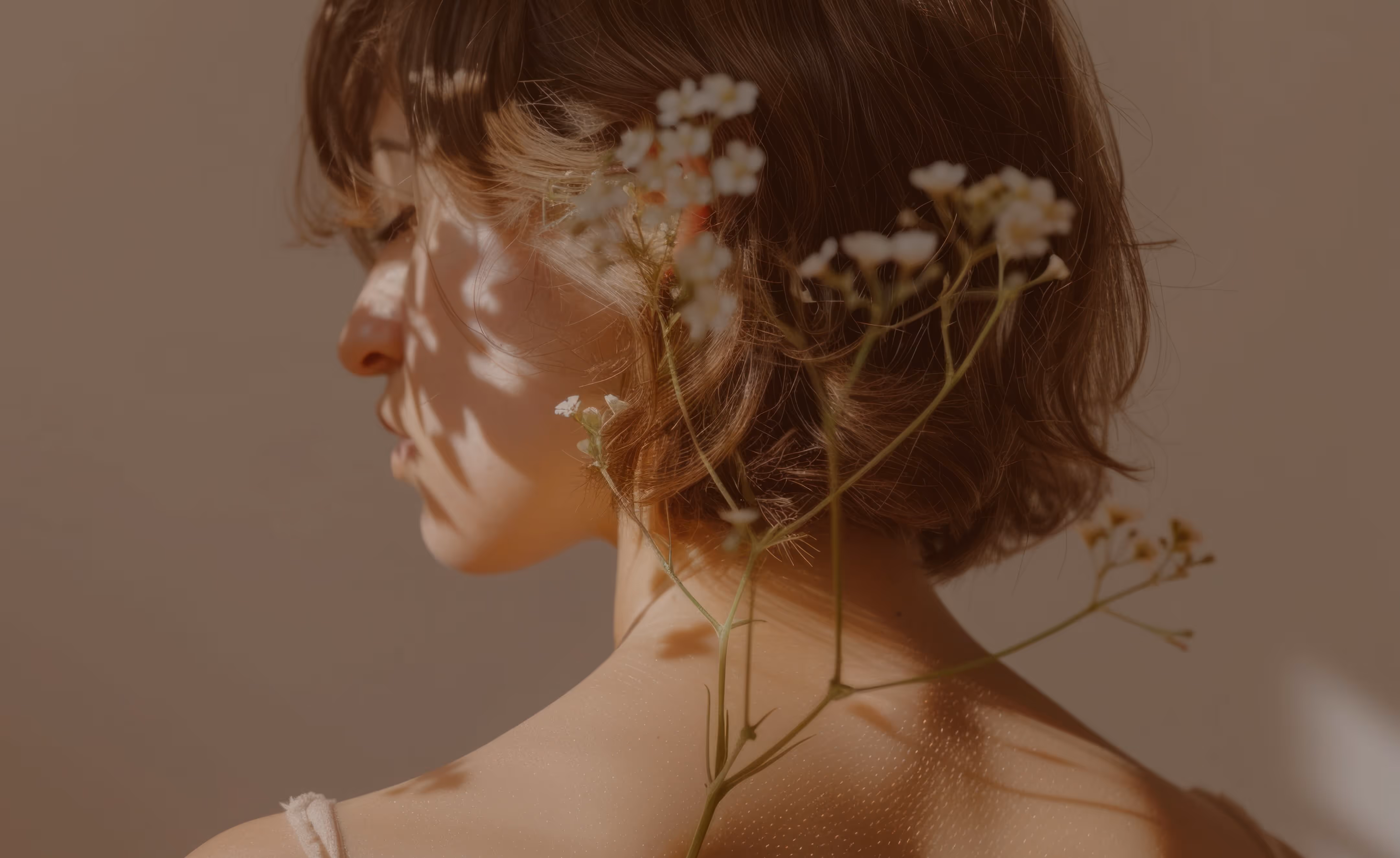 Profile of a person with short brown hair resting their head against a stem of small white flowers casting shadows.