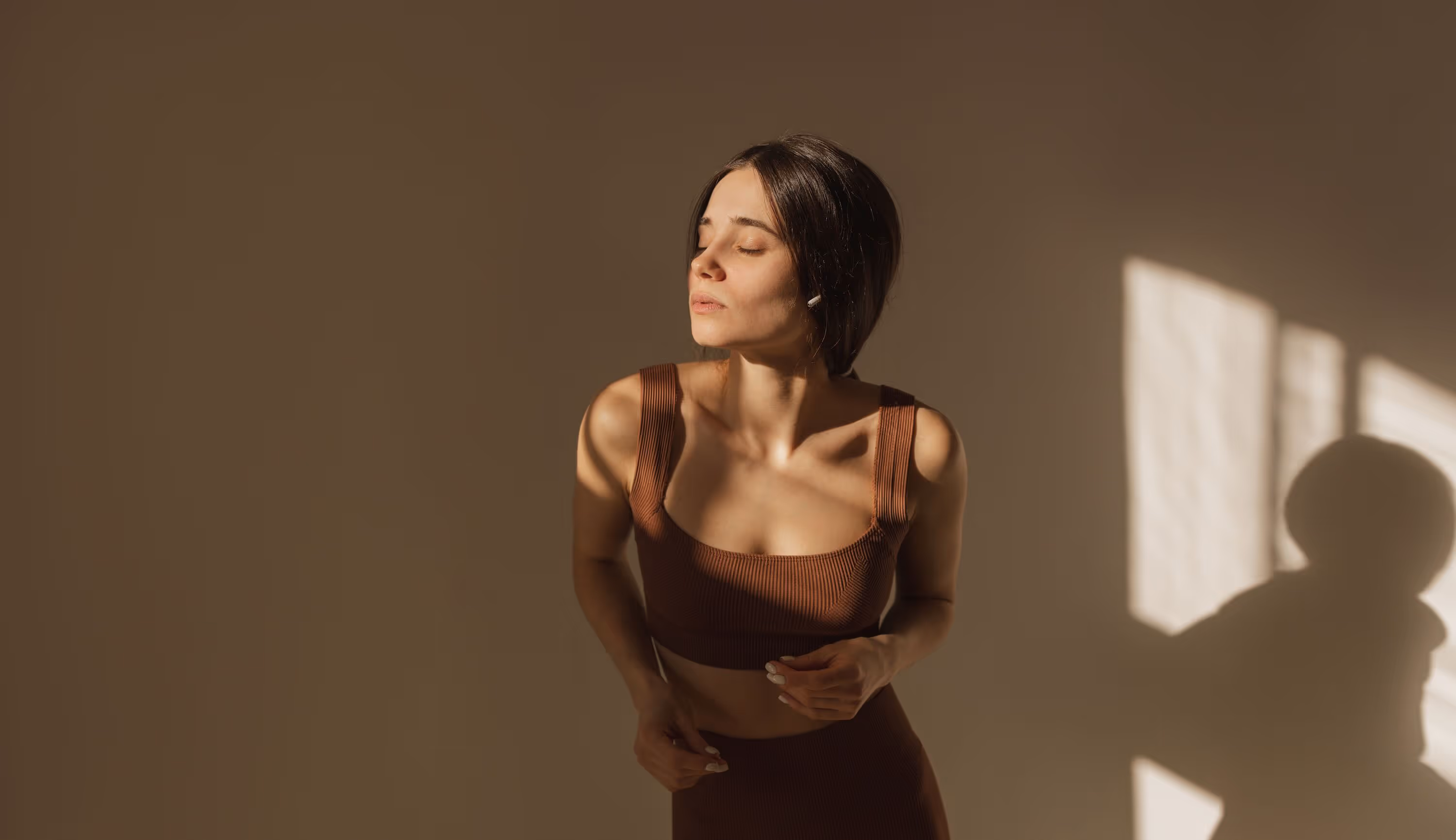 Woman with short dark hair wearing a brown sleeveless top basking in warm sunlight with her eyes closed.
