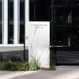 Exterior view of the Langham hotel entrance, featuring a clear signage amidst surrounding greenery.