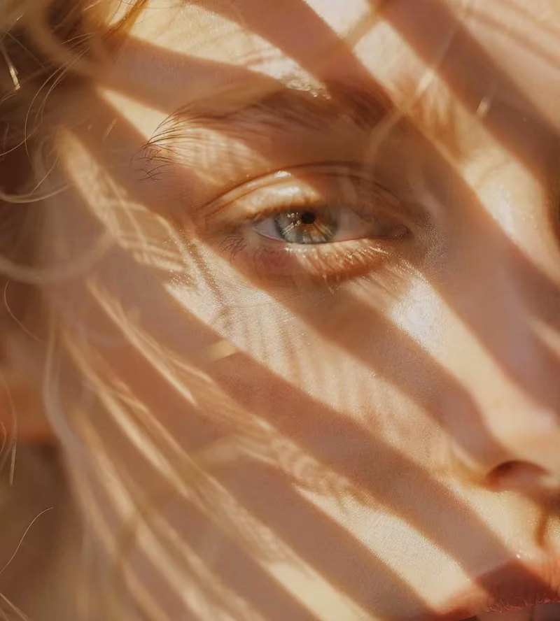 Close-up of a person's face with light and shadow patterns across their eye and skin.