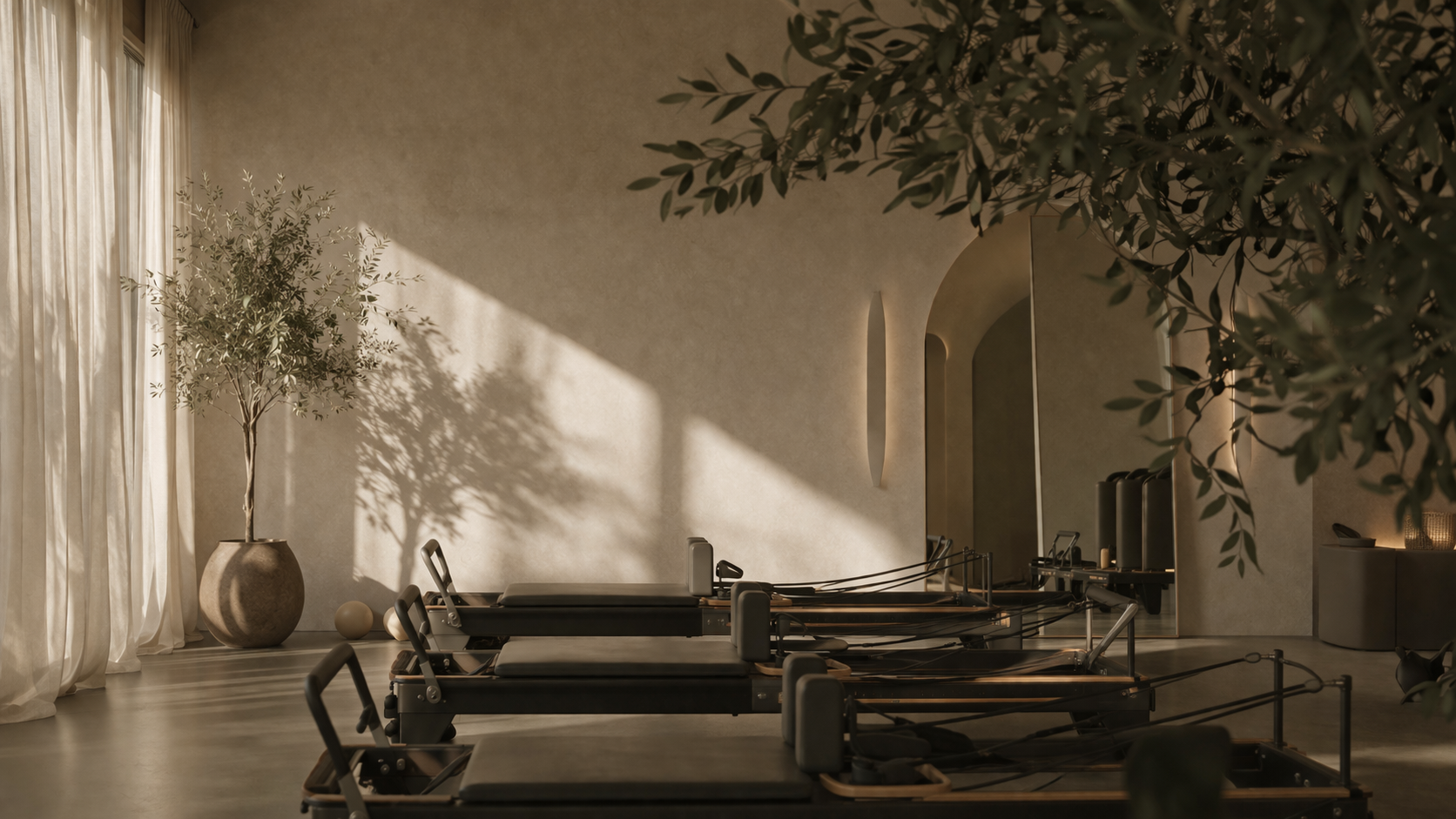 Minimalist Pilates studio with reformer machines, large potted plants, sheer curtains, and warm natural light casting shadows on beige walls.