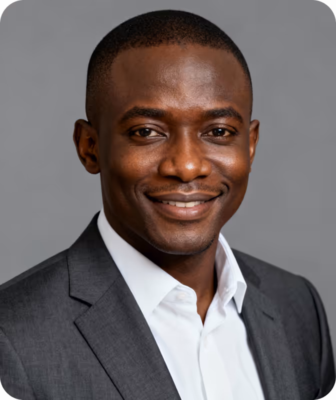 Smiling man wearing a dark gray suit jacket and white shirt against a gray background.