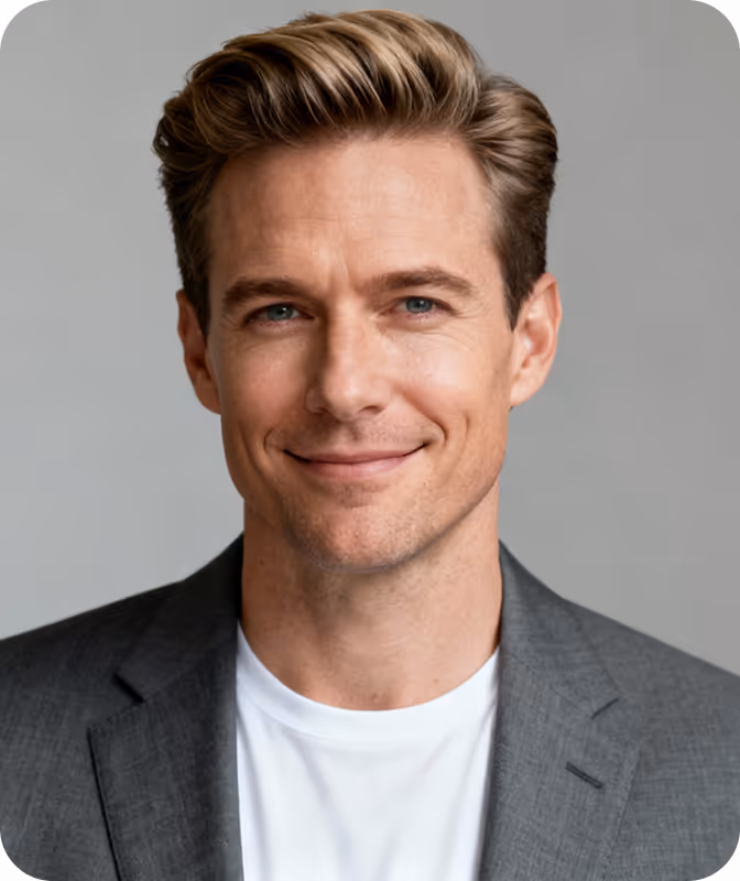 Smiling man with blond hair wearing a gray blazer and white shirt against a gray background.