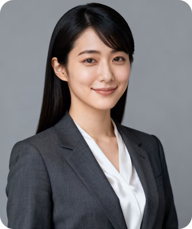 Smiling woman with long black hair wearing a gray blazer and white blouse against a gray background.