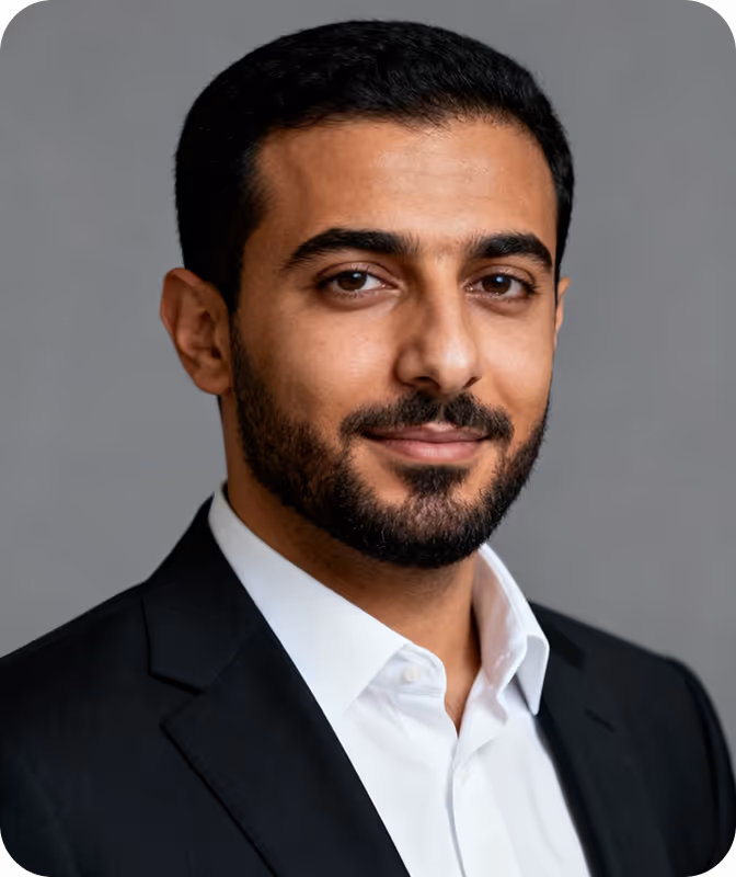 Portrait of a man with short black hair and beard wearing a white shirt and black blazer against a plain gray background.