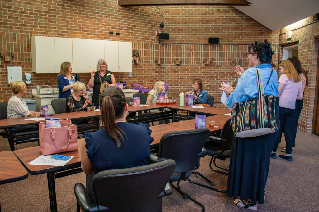 Group of women socializing and drinking tea in a meeting room with brick walls and tables.