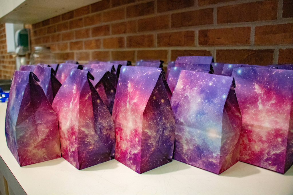 Multiple colorful gift bags with galaxy-themed designs arranged on a white surface.