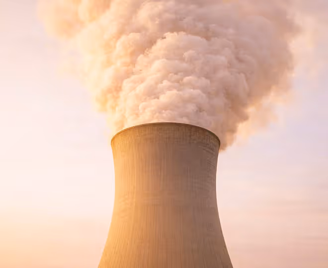 Cooling tower of an industrial plant emitting thick steam into the sky at sunset.