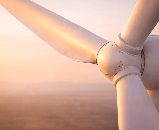 Close-up of a wind turbine's rotor blades with sunlight casting a warm glow.