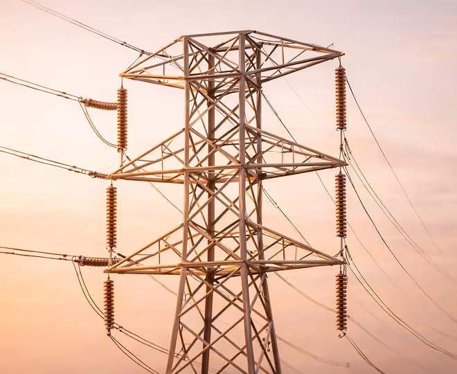 Close-up of an electrical transmission tower with multiple insulators and power lines against a soft, pastel sky at sunset.