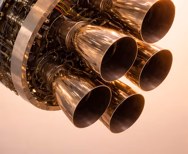 Close-up view of five metallic rocket engine nozzles with intricate piping and wiring.