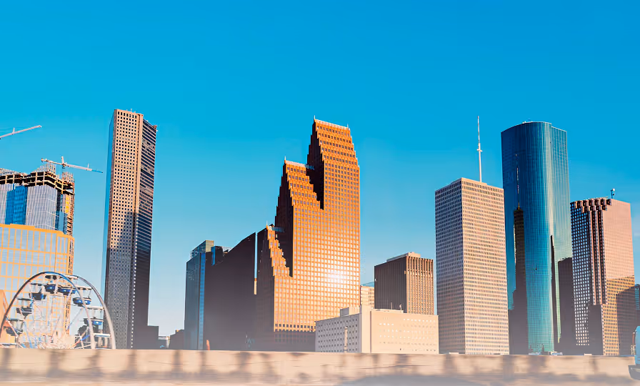 Downtown city skyline with modern skyscrapers and a ferris wheel under a clear blue sky.