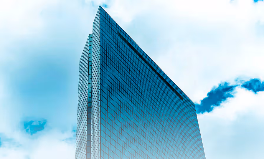 Low-angle view of a modern glass skyscraper against a cloudy blue sky.