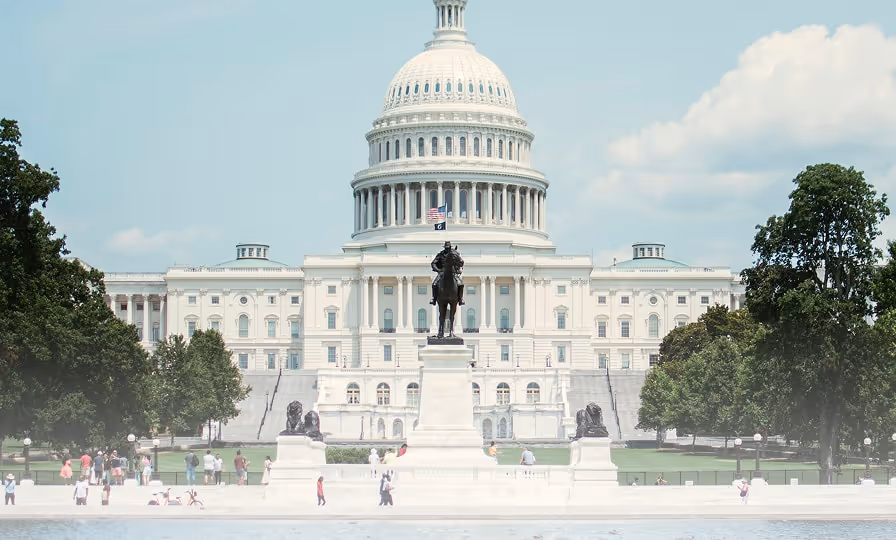 United States Capitol building with a horse-mounted statue and visitors in the foreground on a sunny day.