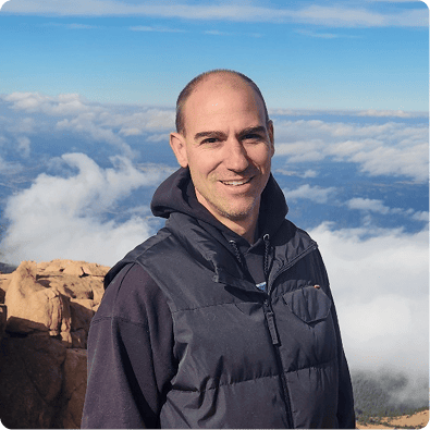 Portrait of Rob Galfi, Co-Founder at Impact by Insight, smiling outdoors on a mountain landscape above the clouds, accompanied by a bio highlighting his 25+ years of experience as an end-to-end data analyst with a focus on data architecture and process efficiency.
