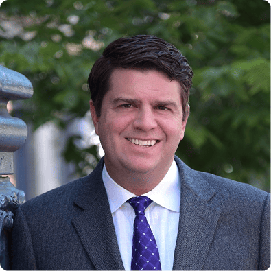 Portrait of Jason Phillips, Co-Founder at Impact by Insight, smiling in a suit and tie outdoors, accompanied by a bio highlighting his 25+ years of experience in analytics, KPI development, and building high-performing analytical teams.