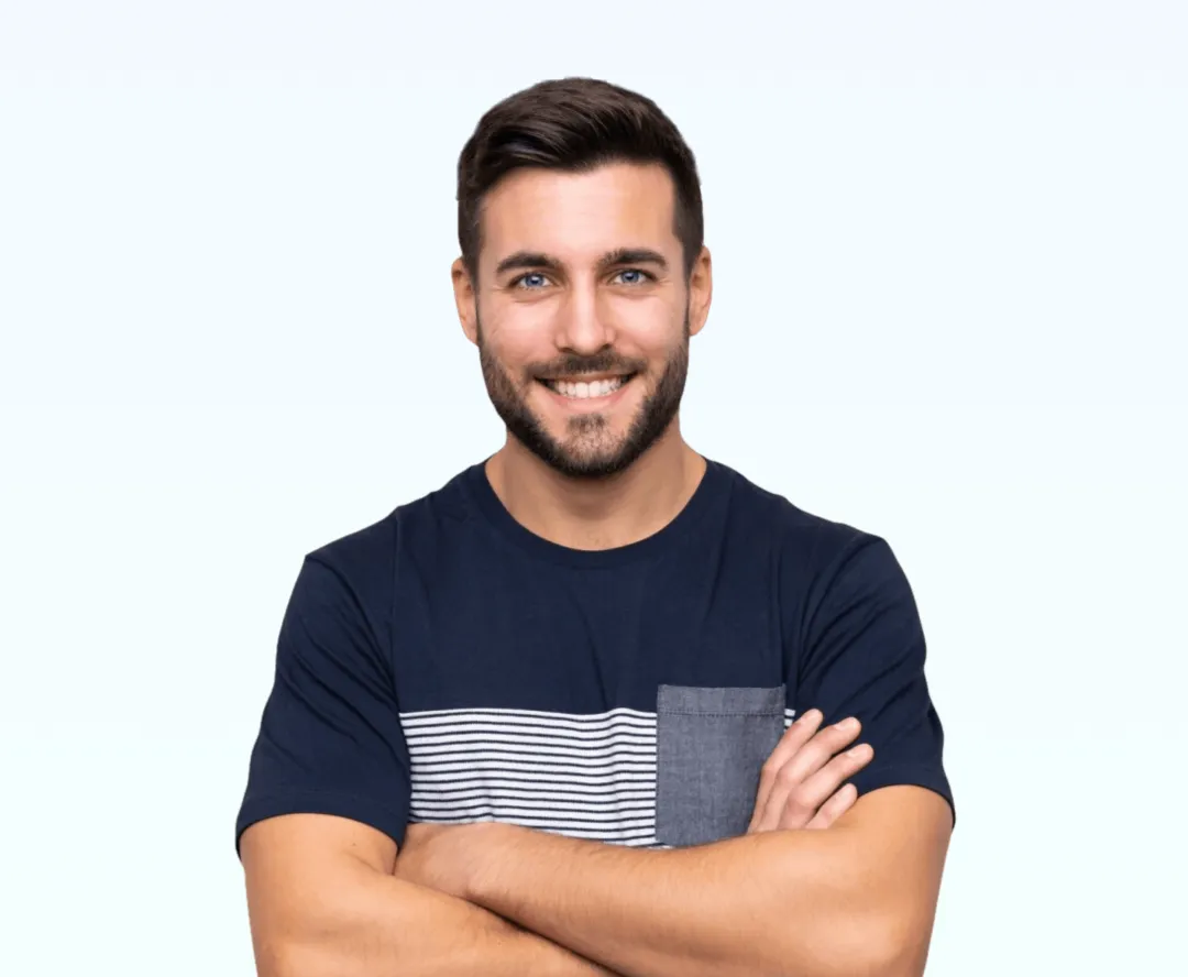 Smiling man with short dark hair and beard, wearing a navy blue T-shirt with a horizontal striped pocket, arms crossed.