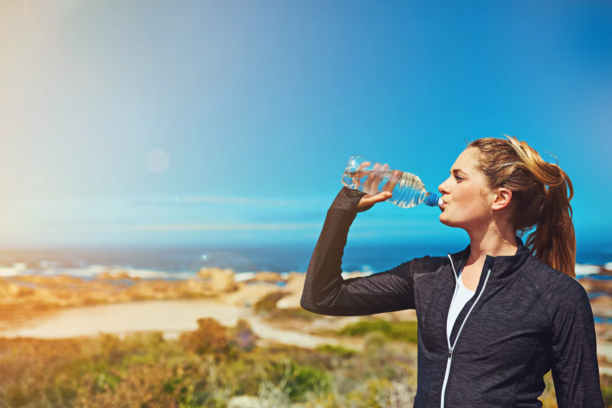 woman on the beach drinking a bottle of water.