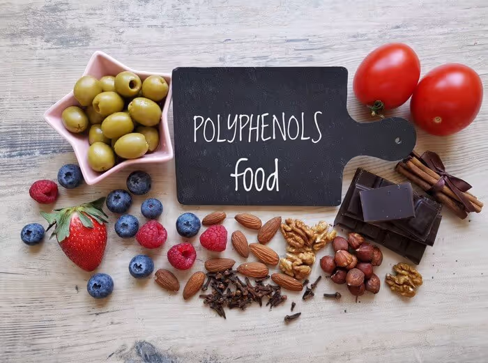 Assorted polyphenol-rich foods including olives, berries, nuts, chocolate, and tomatoes with a chalkboard labeled 'Polyphenols Food.