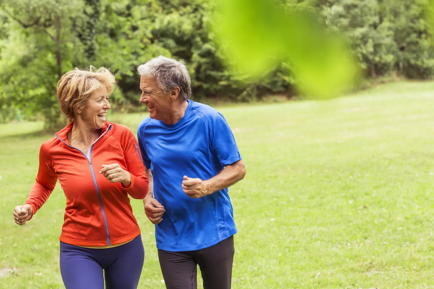 Smiling older couple jogging side by side through a green park to support heart health