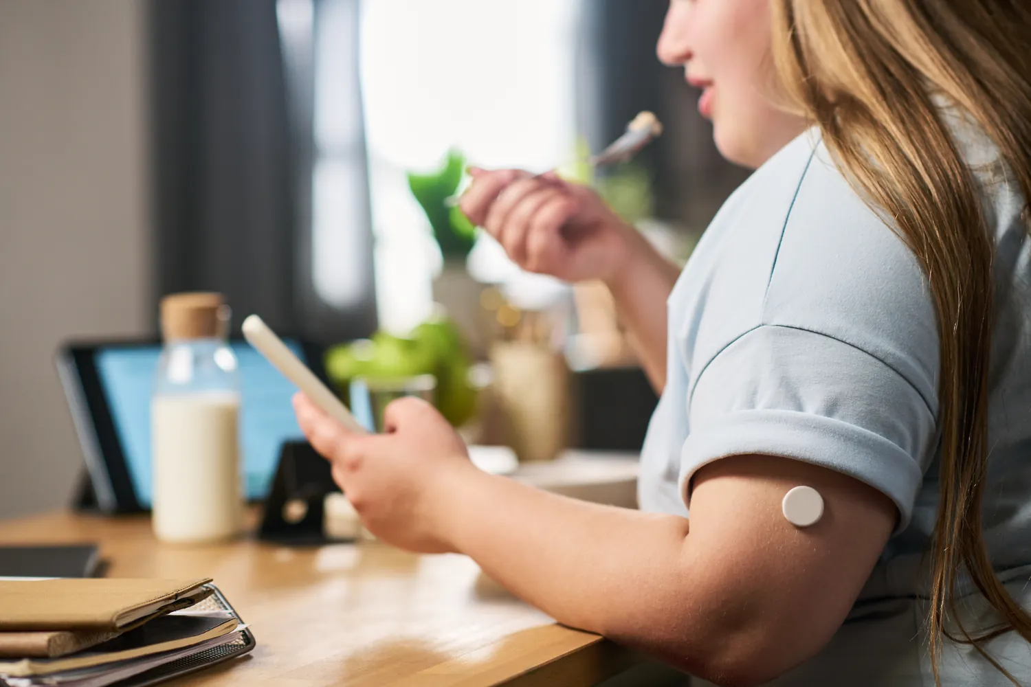 Woman wearing a continuous glucose monitor on her arm checks her phone while eating a meal