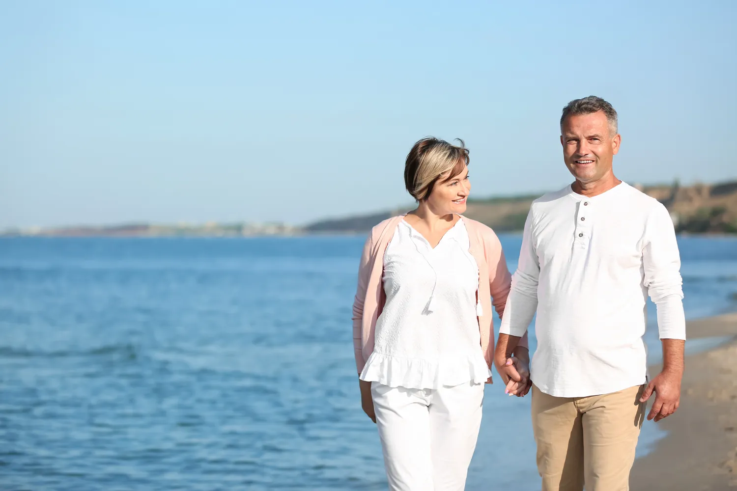 Mature couple holding hands and walking along the beach on a sunny day