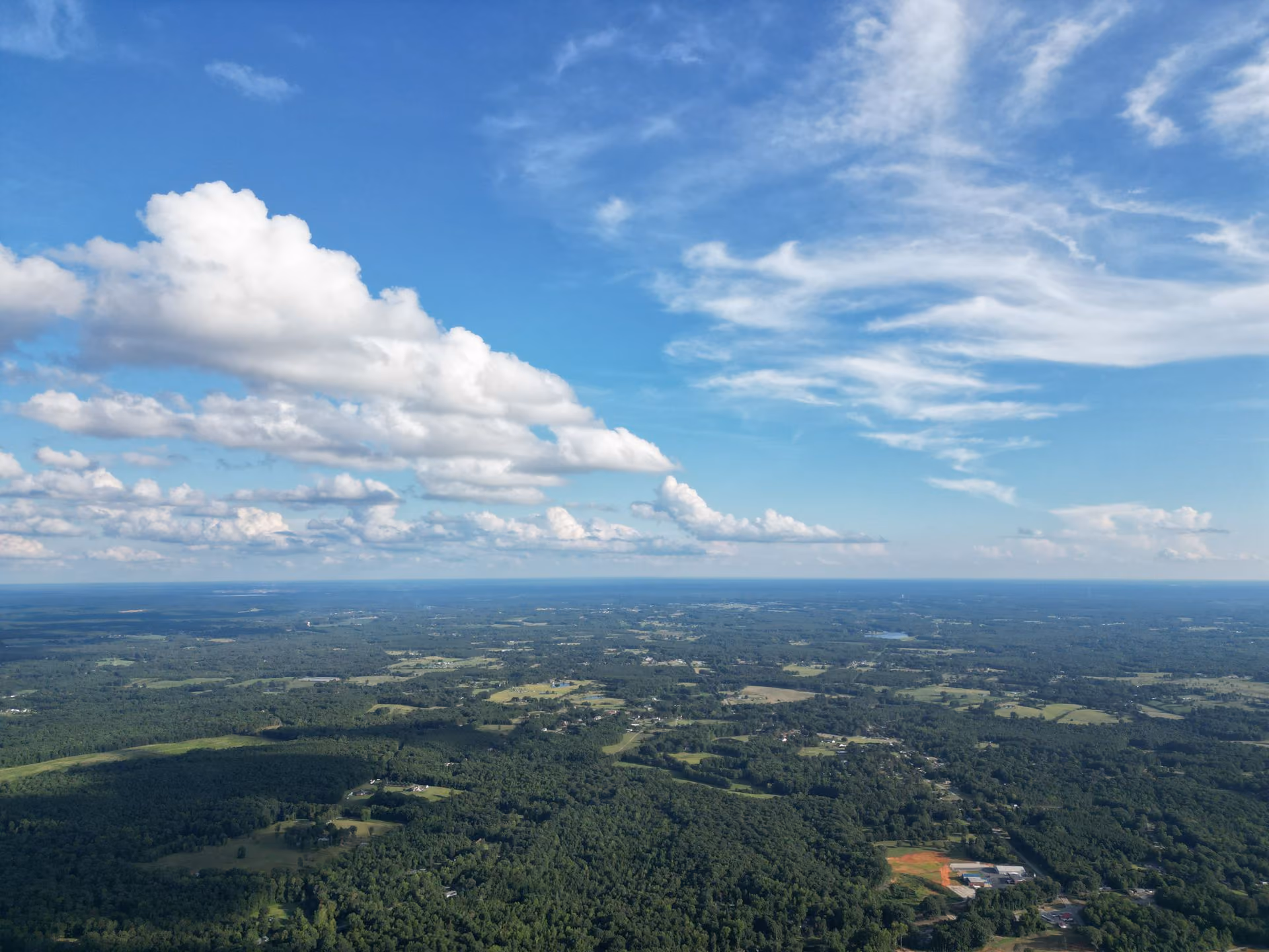 Aerial view of green forests and fields under a blue sky with white clouds.