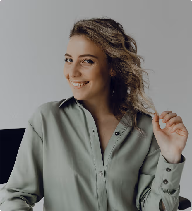 Smiling woman with wavy hair wearing a light green button-up shirt, holding a strand of her hair.