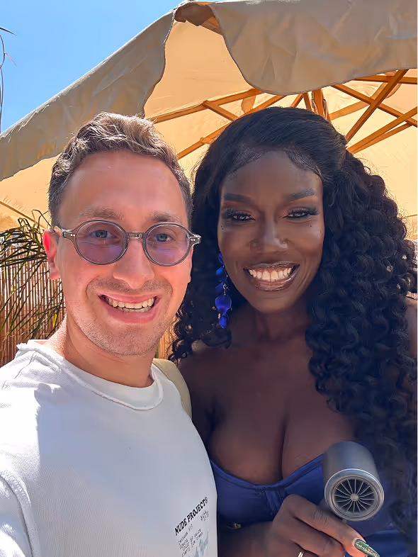 Smiling man with glasses in a white shirt posing with a smiling woman with long curly hair and blue earrings under a canopy.