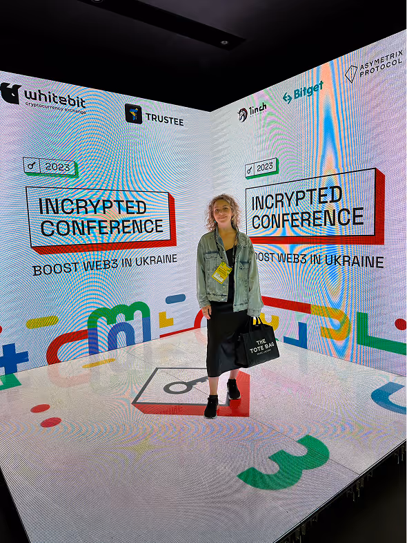 A woman standing inside a bright digital display area featuring logos and text for the 2023 Incrypted Conference boosting Web3 in Ukraine.