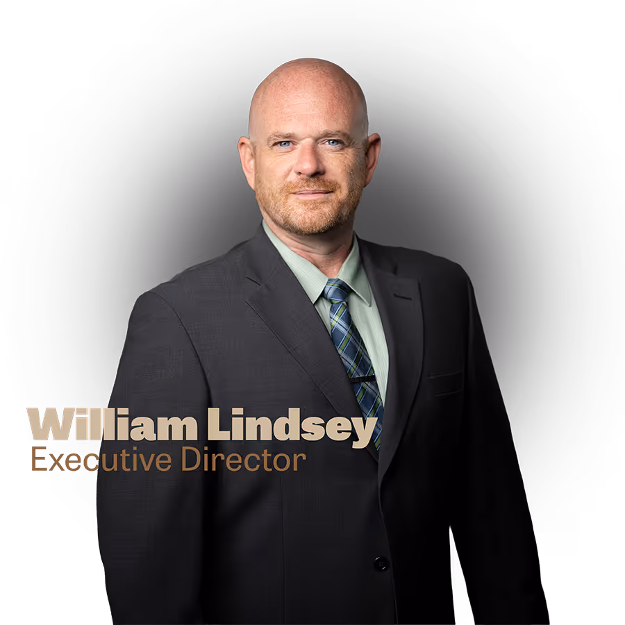 Portrait of William Lindsey in a suit and tie, titled Executive Director against a dark background.