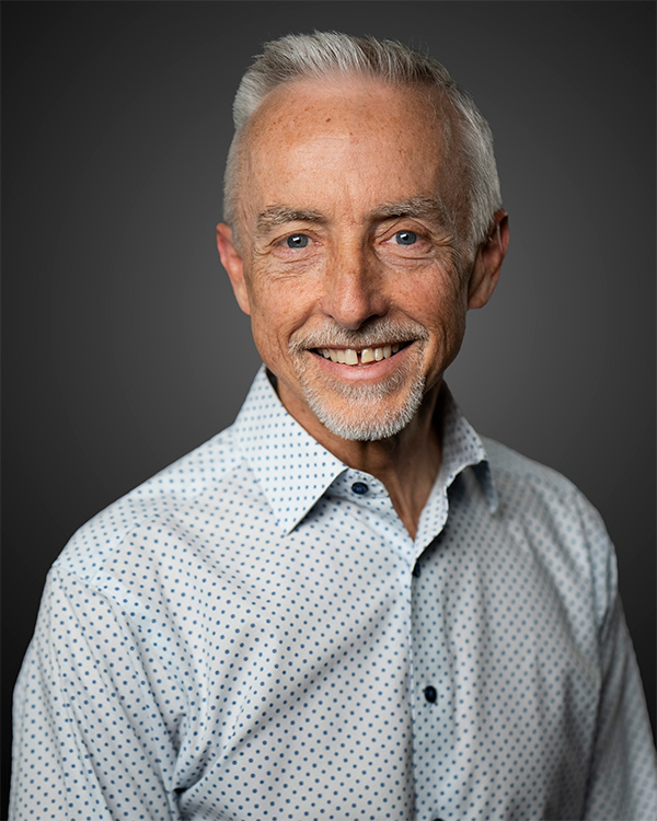 Smiling elderly man with white hair and beard wearing a white shirt with blue dots.