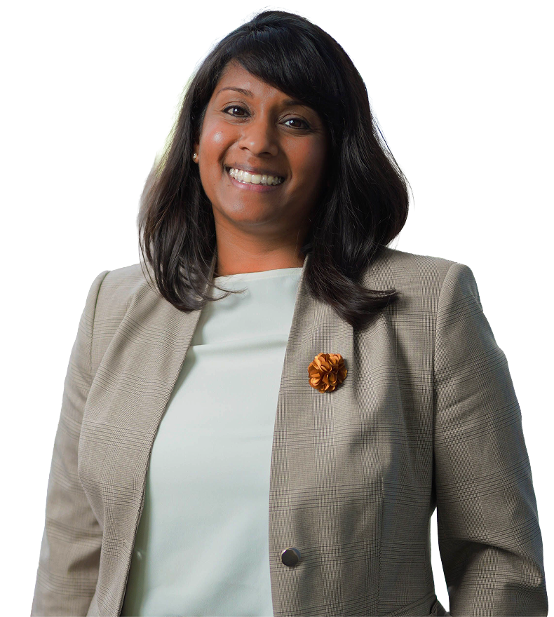 Smiling woman with medium-length dark hair wearing a light-colored top and a beige blazer with a decorative orange flower pin.