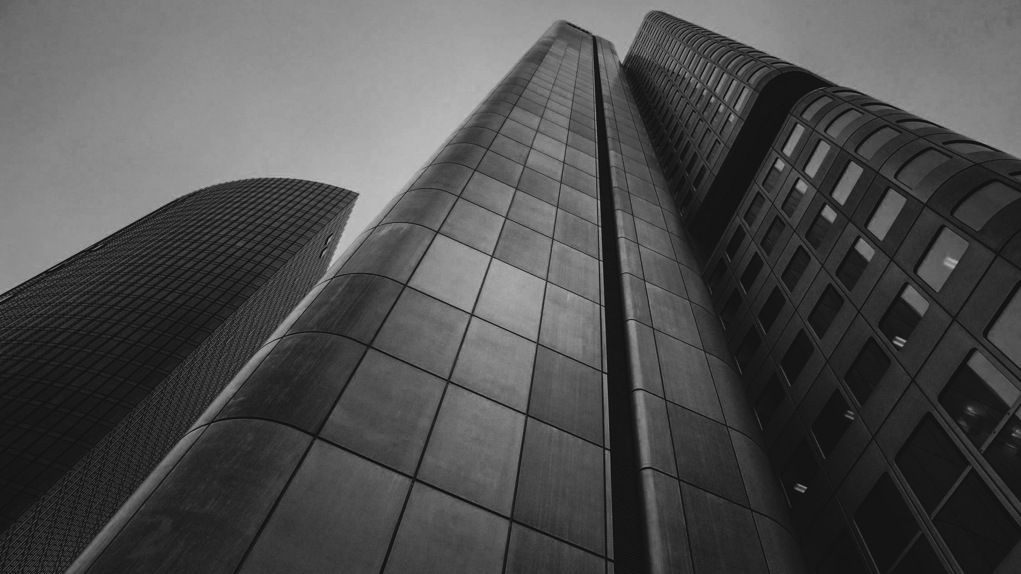 Black and white photo looking up at three modern skyscrapers with glass and metal facades.