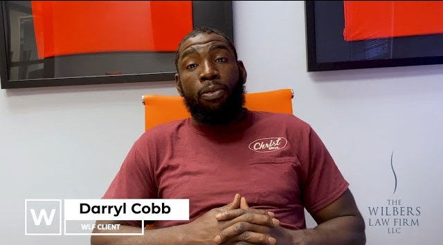 Man with a beard sitting in an orange chair, wearing a maroon shirt with the logo 'Christ Bros.', with text overlay identifying him as Darryl Cobb, WLF client.