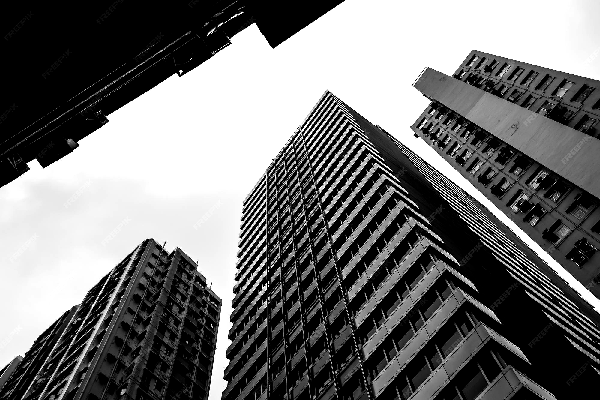 Black and white photo looking up at three tall urban apartment buildings with windows and balconies.