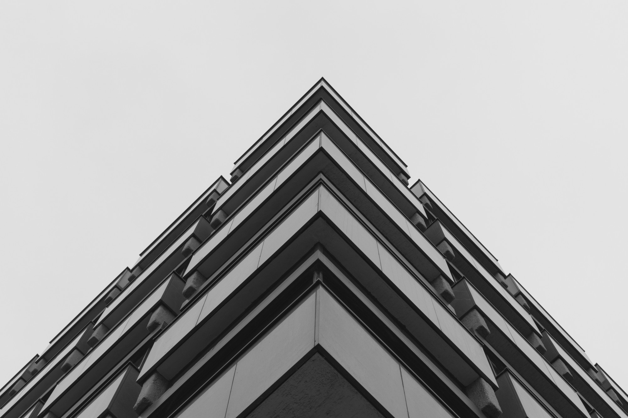 Black and white photo looking up at the sharp corner of a modern multi-story building against a blank sky.