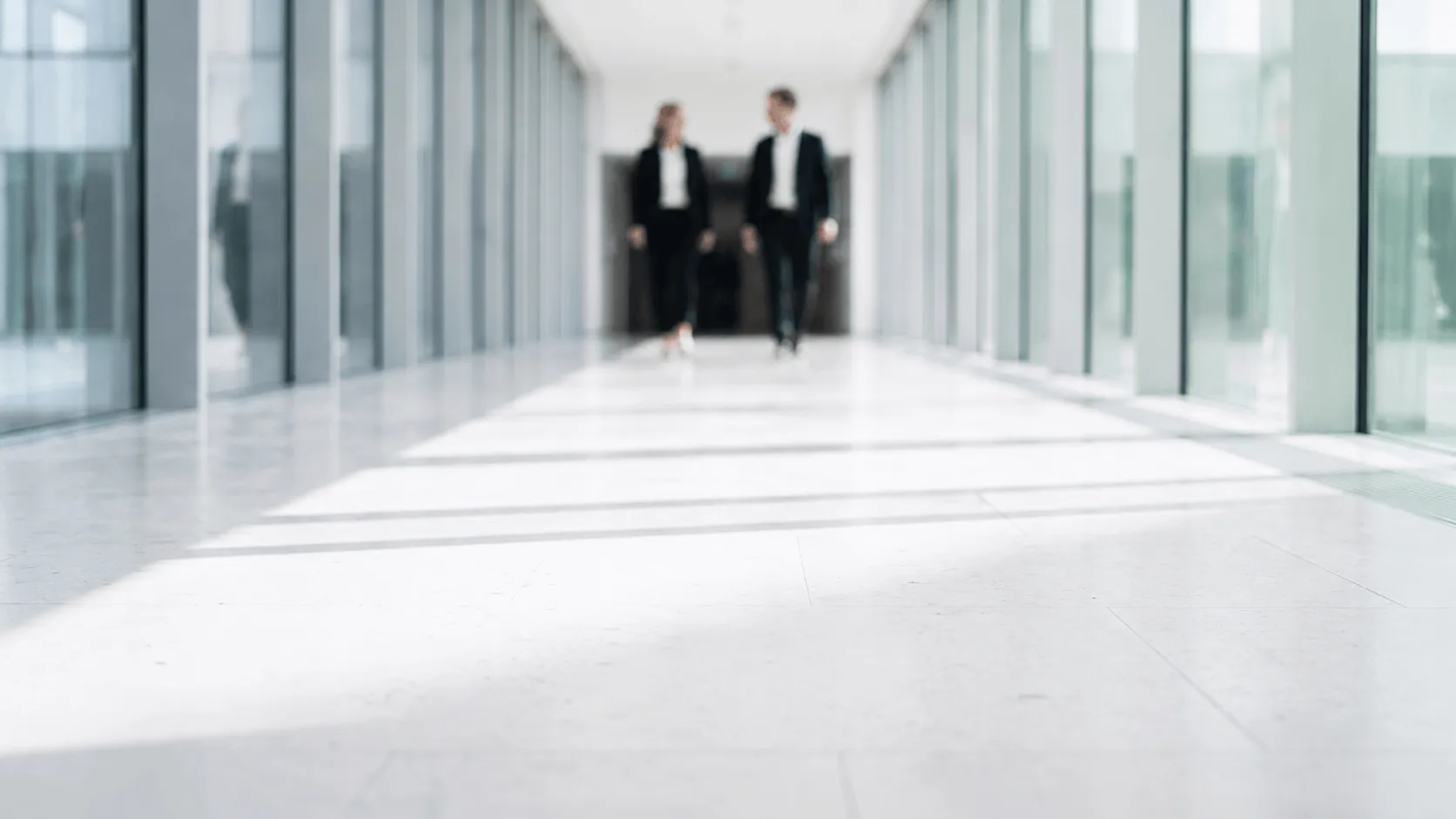 Two business professionals walking and talking in a bright modern glass corridor.