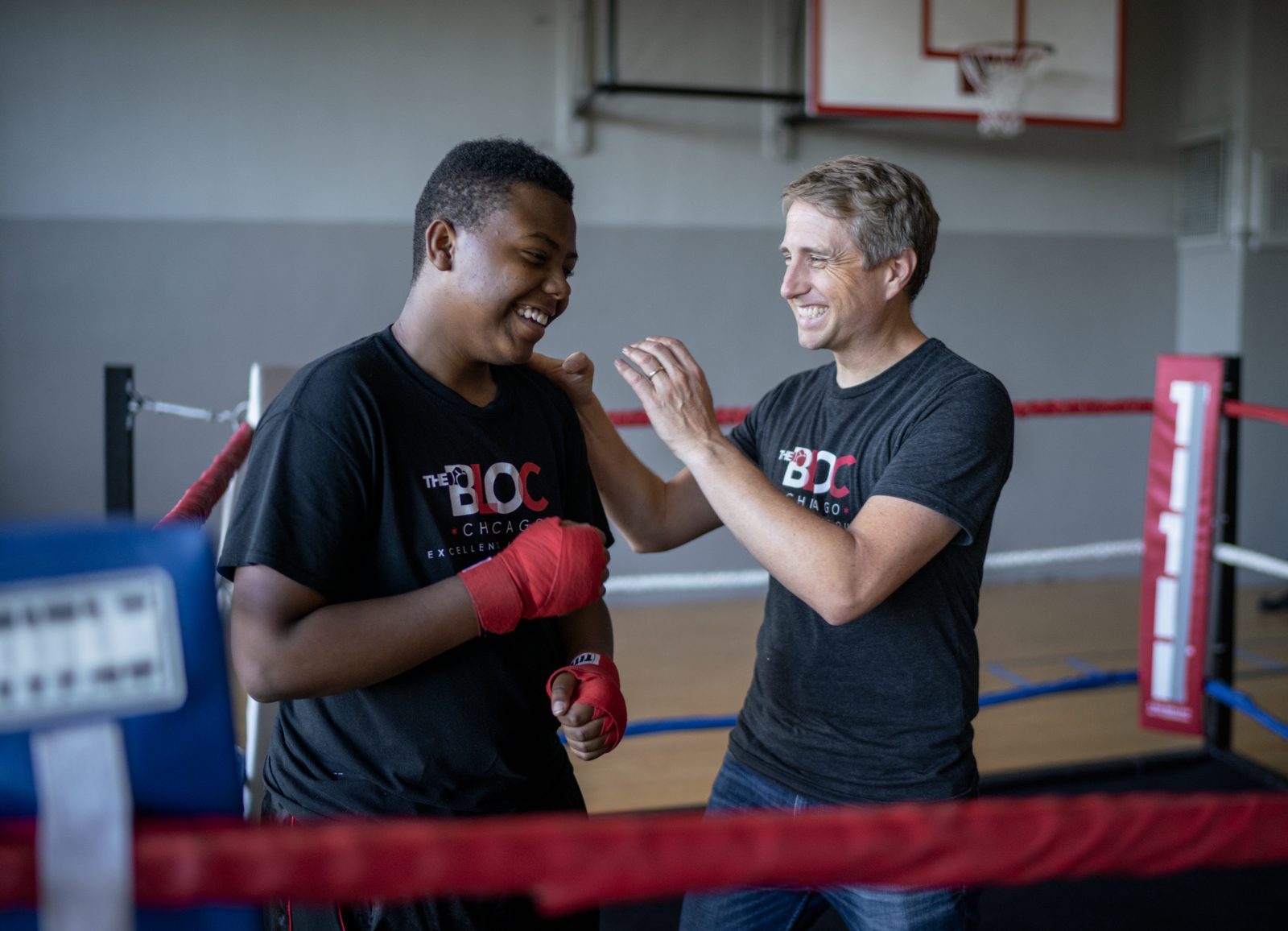 A coach and a young boxer laughing together in a gym