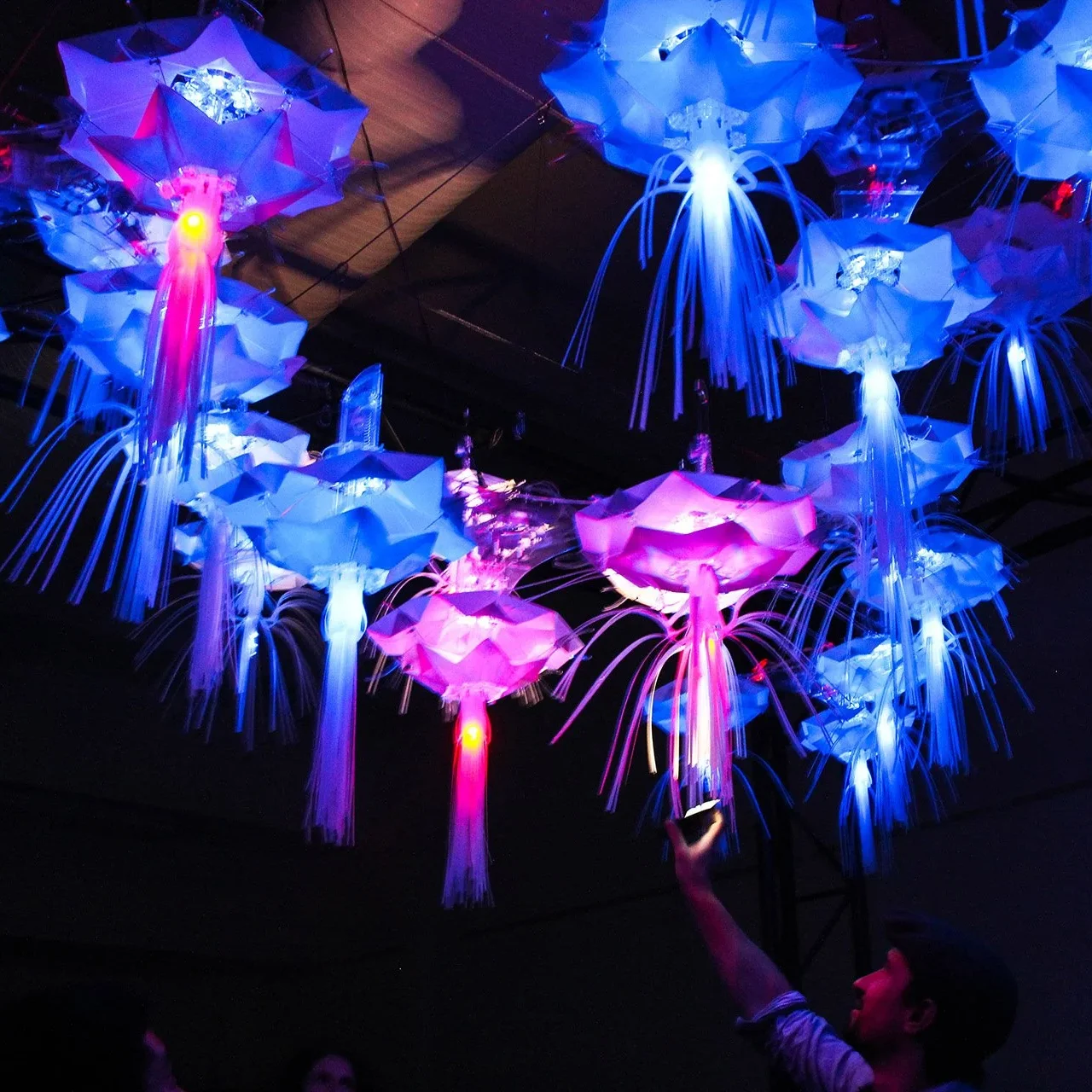 Flock of glowing artificial jellyfish hovering around a person interacting with light