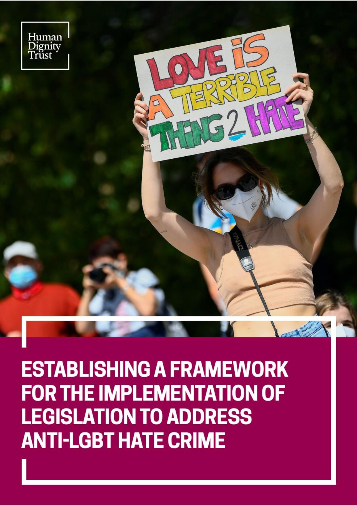 Cover of the Human Dignity Trust report 'Establishing a framework for the implementation of legislation to address anti-LGBT hate crime', showing a protester holding a hand-lettered placard reading 'Love is a terrible thing to hate'.